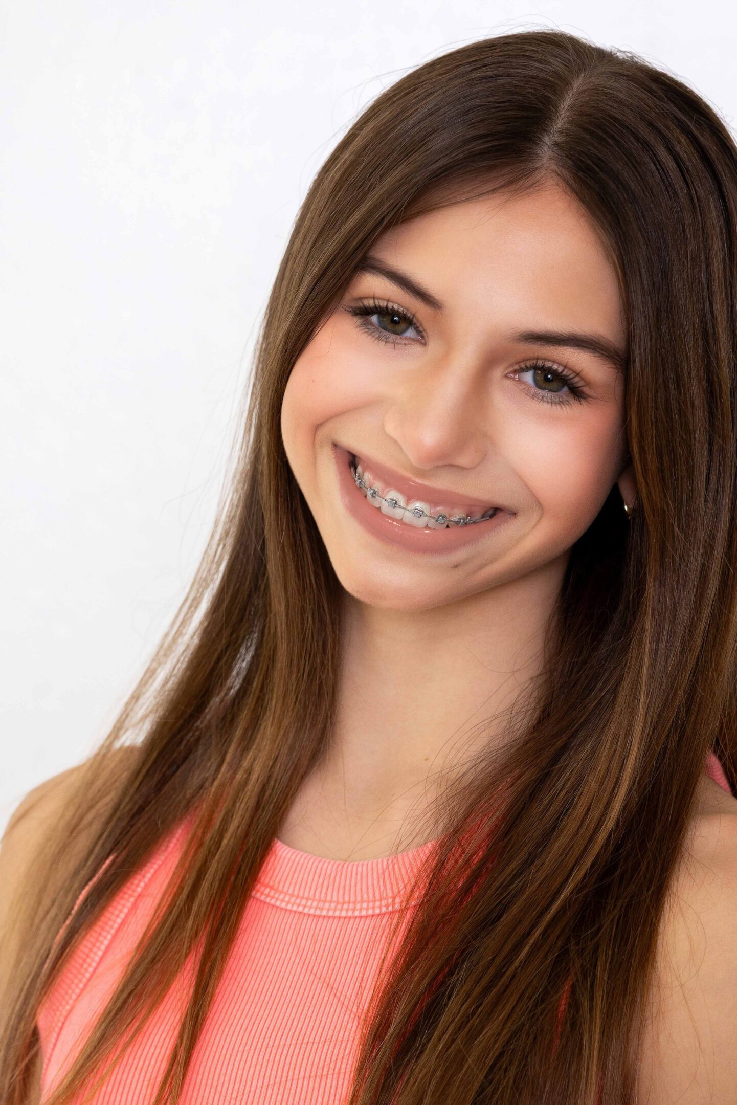Smiling teenage girl with braces and long brown hair wearing a coral top.